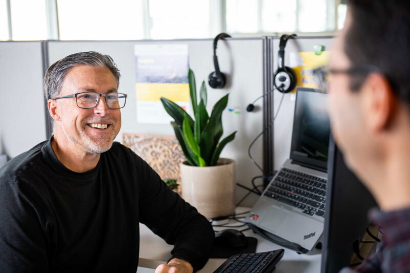 smiling man in black shirt in an office looking at man across the table