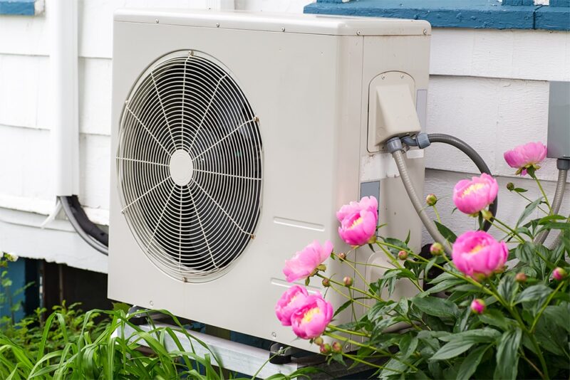 Air conditioning/ Heat pump unit on the side of a home among the flowers.